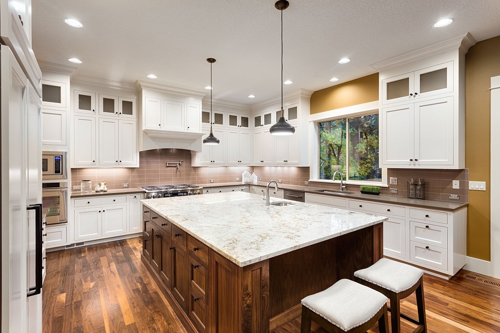 Large Kitchen Interior with Island, Sink, White Cabinets, Pendant Lights, and Hardwood Floors in New Luxury Home